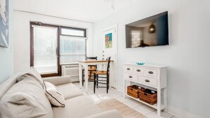 A modern living room with a sofa, a dining table with chairs, a TV mounted on the wall, and a white cabinet with baskets. - Why Knot Getaway...Rooftop with WaterView!  Unit D (Beaufort)