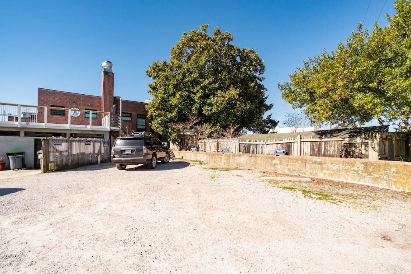 A gravel parking area with a vehicle, a brick building with a water tower, and a large tree.
