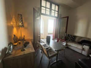A compact living space with a dining table, two chairs, a sofa, and a large window.