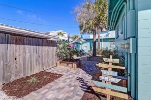 Explore the serene backyard oasis with a paved pathway leading to a fence, surrounded by lush plants and a palm tree.