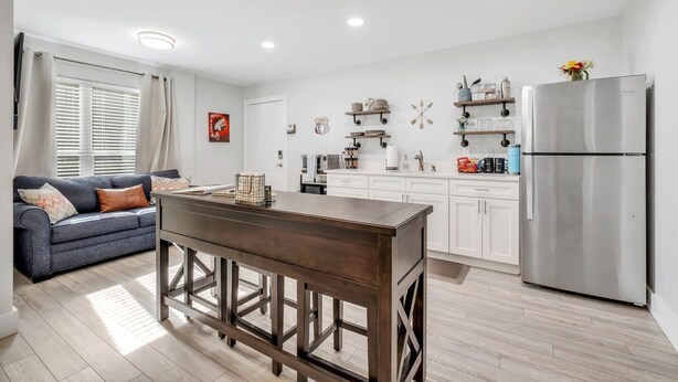 Une cuisine moderne avec des meubles blancs, un réfrigérateur en acier inoxydable et un coin bar doté d’une table en bois.