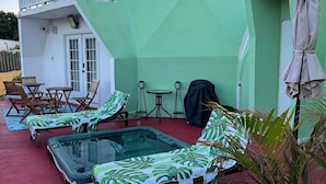 Un edificio verde con balcón, zona de piscina con sillones de descanso y un patio cubierto.