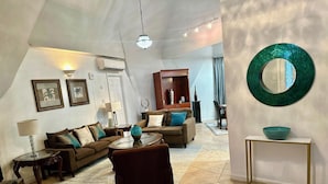Una sala de estar con sofá, sillón, mesa de centro y elementos decorativos. Cuenta con una zona de comedor con mesa y sillas.