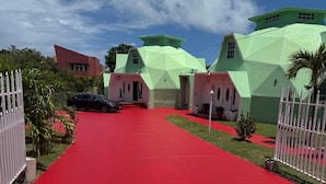 Un camino conduce a un edificio con un diseño geométrico único, una alfombra roja y una cerca blanca.