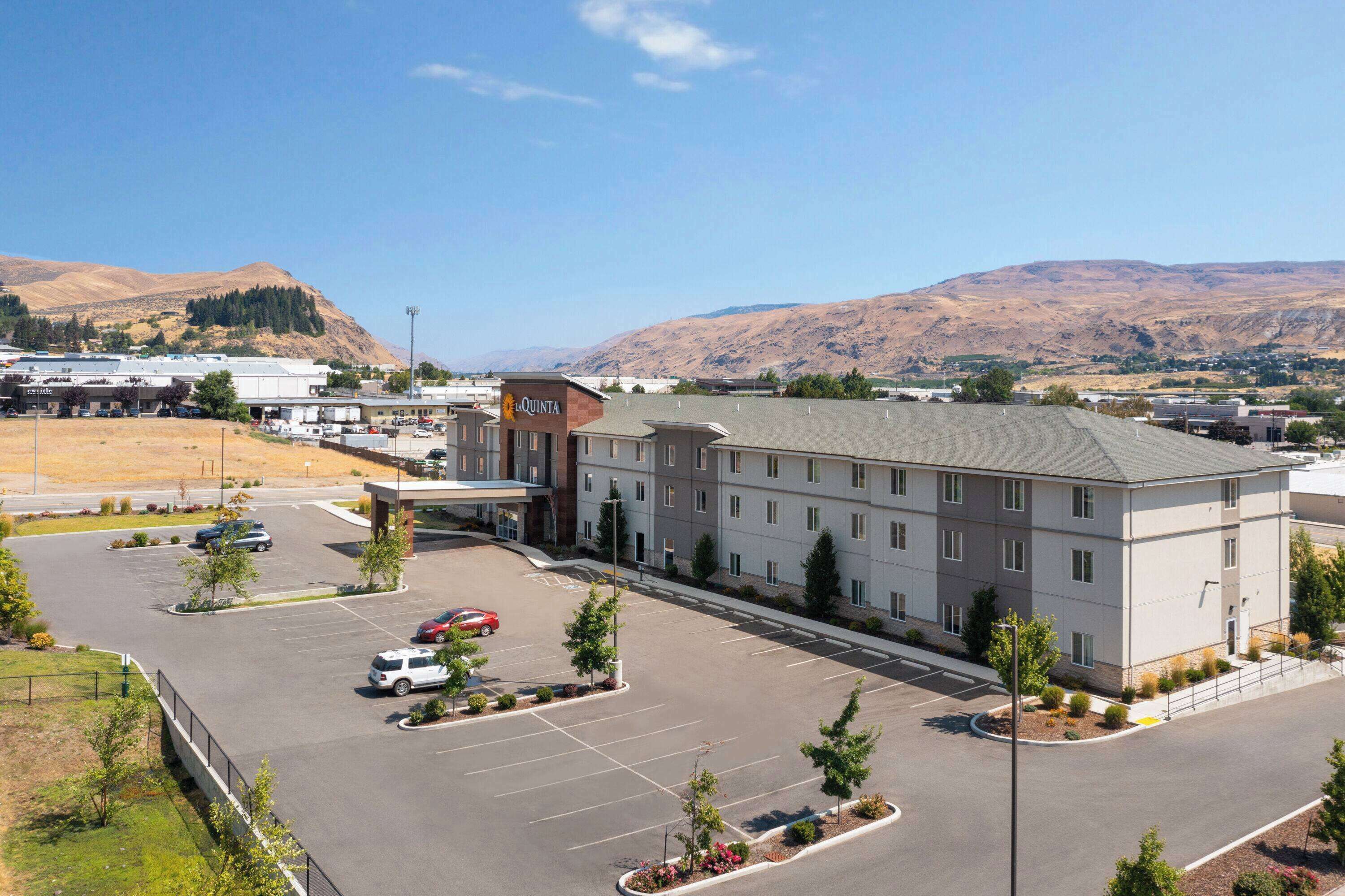 A hotel with a parking lot, a building with a flat roof, and a mountainous backdrop.