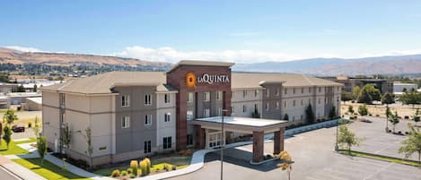 A hotel with a prominent 'La Quinta' sign, a covered parking area, and a view of distant hills.