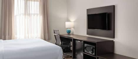 A hotel room with a bed, desk, chair, TV, and a lamp.