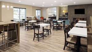 A modern dining area with multiple tables and chairs, a bar area, and a fireplace. - La Quinta Inn & Suites by Wyndham Wenatchee (Wenatchee)