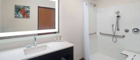 A bathroom with a white sink, a mirror, a shower with a grab bar, and a towel rack.