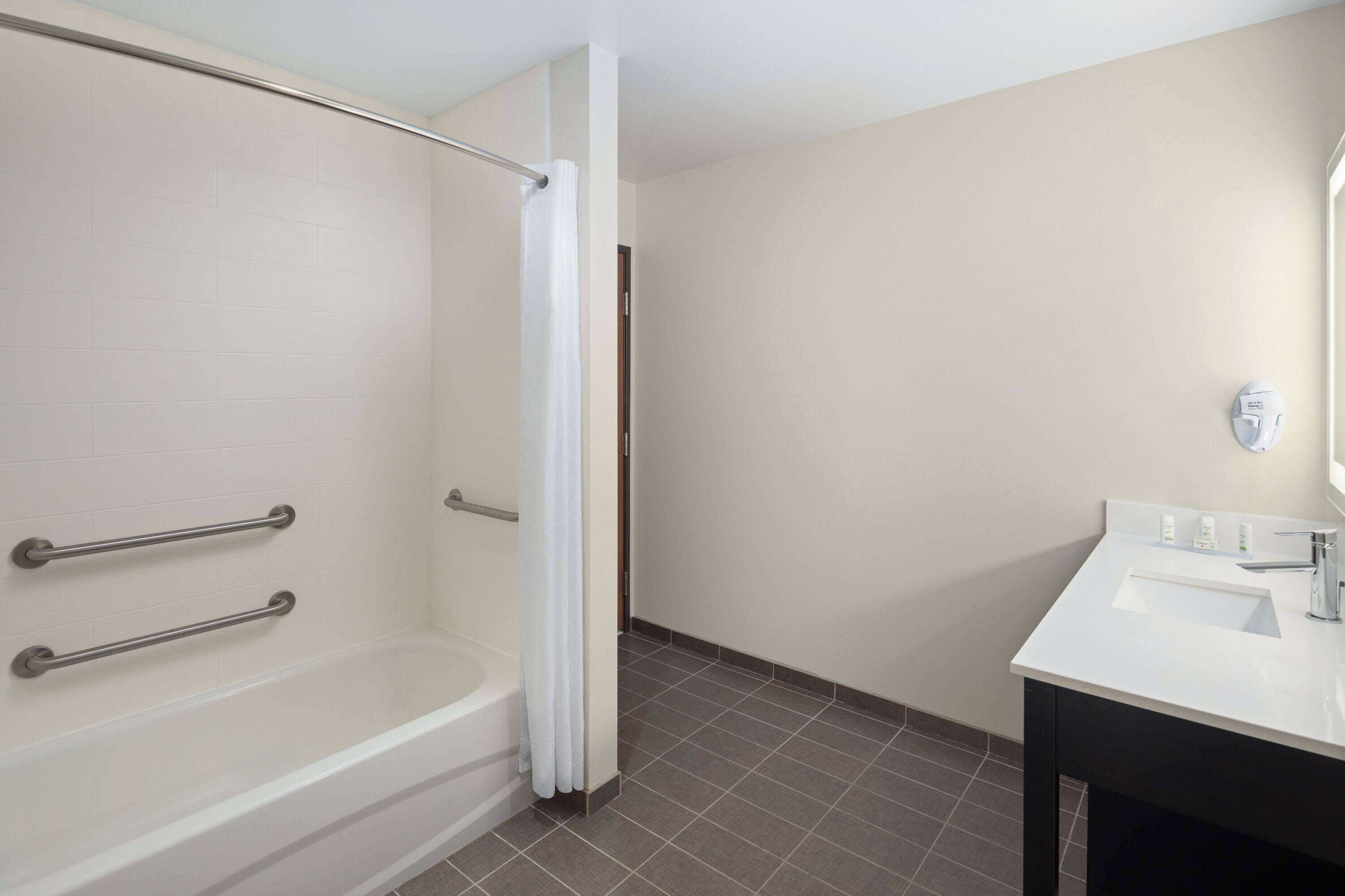 A bathroom with a bathtub, a shower curtain, a sink, and grab bars.