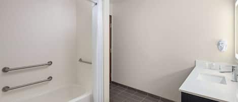 A bathroom with a bathtub, a shower curtain, a sink, and grab bars.