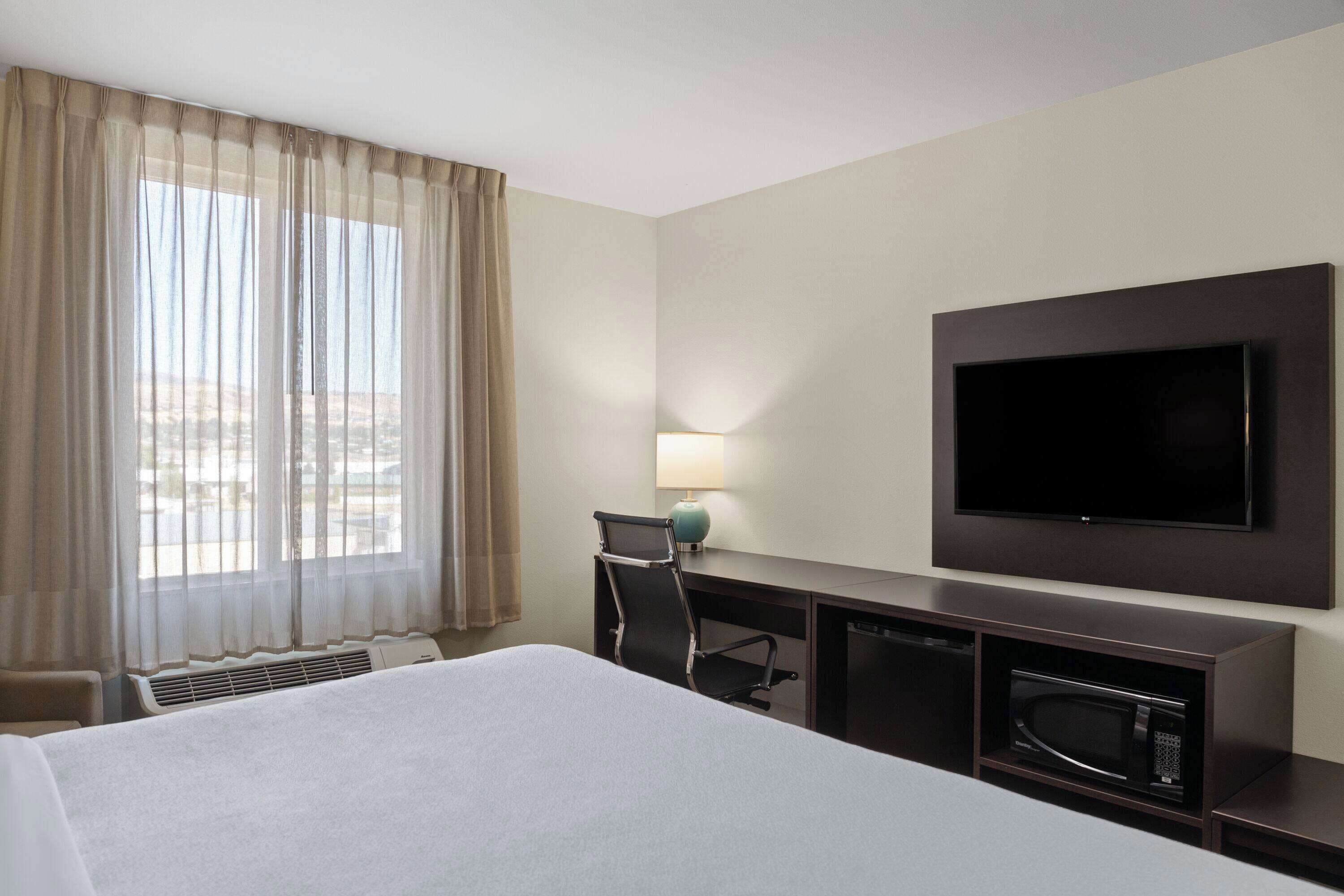 A hotel room with a bed, a desk, a television, and a window with curtains.