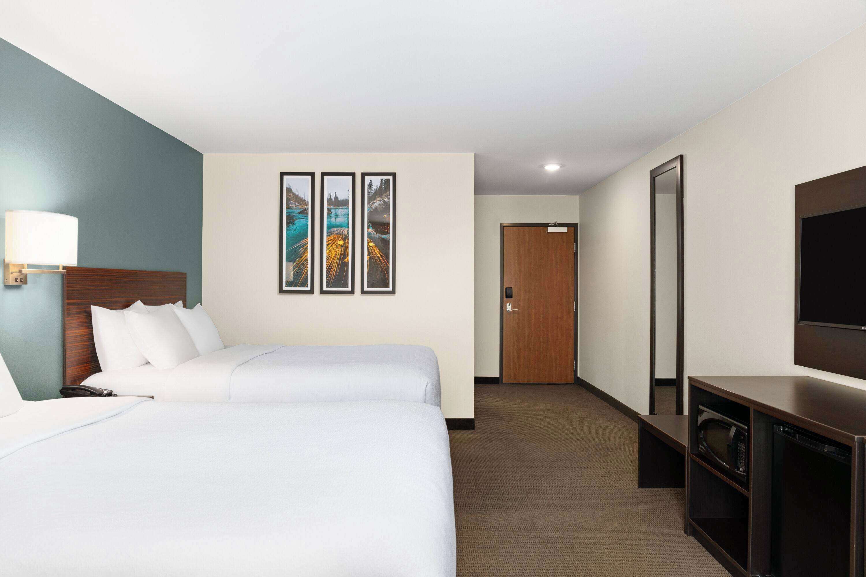 A hotel room with two beds, a TV, a desk, and a door leading to another room.