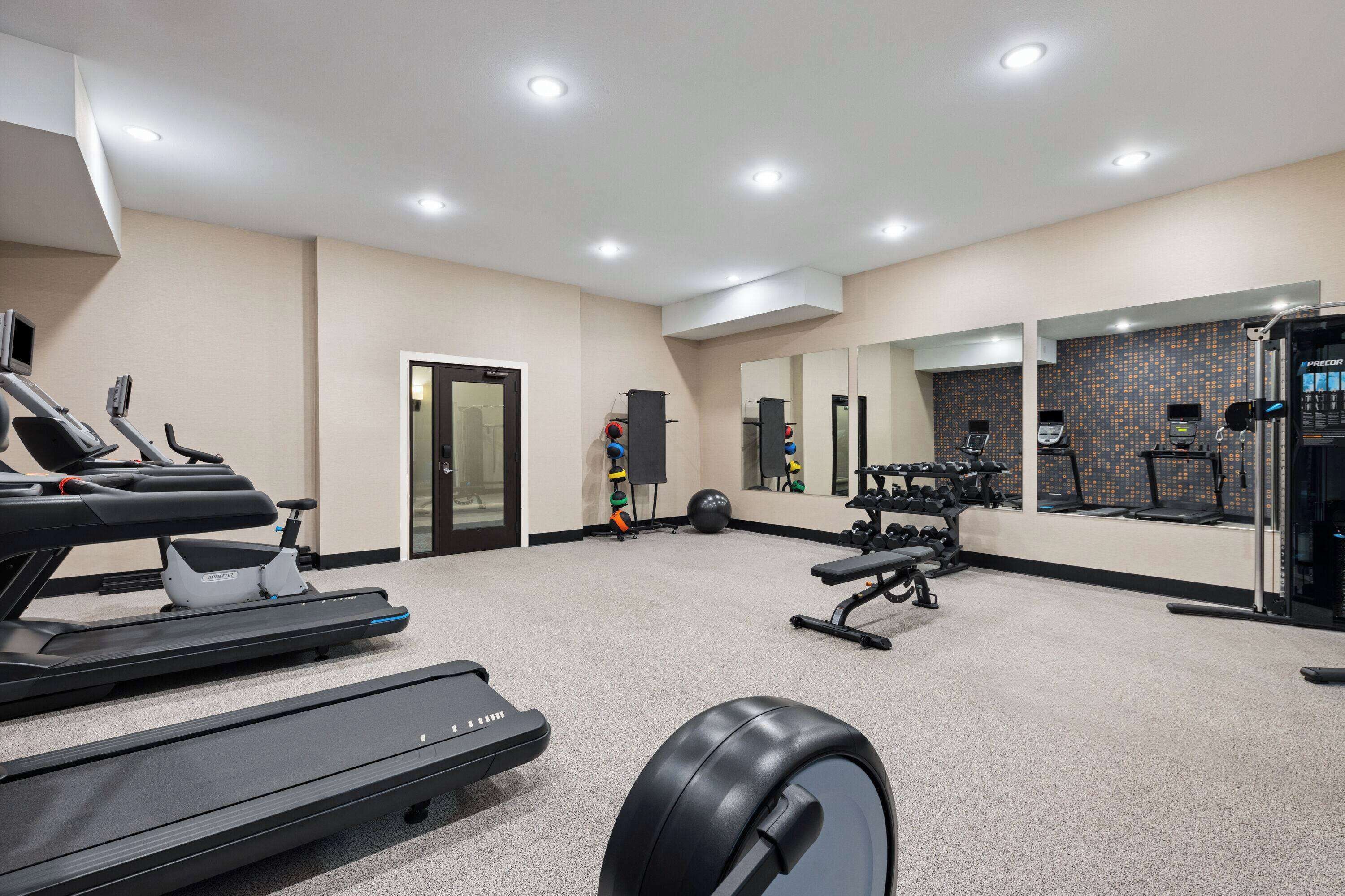 A gym with treadmills, weight machines, and a mirrored wall.