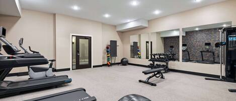 Une salle de sport équipée de tapis de course, d’appareils de musculation et d’un mur recouvert de miroirs.