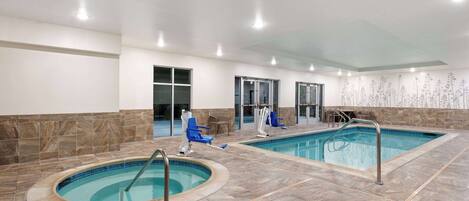 An indoor swimming pool area with two pools, lounge chairs, and a seating area.