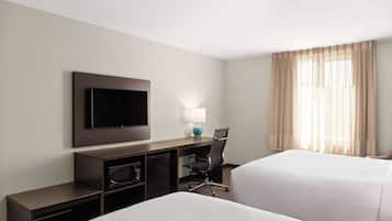 Una habitación de hotel con dos camas, un escritorio, un televisor de pantalla plana, una lámpara y una silla.