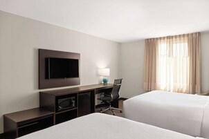 Una habitación de hotel con dos camas, un escritorio, un televisor de pantalla plana, una lámpara y una silla.