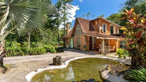 A rustic house with a tiled roof, surrounded by lush greenery and a small pond. - Boutique chalet amidst the Atlantic rainforest. (PETRÓPOLIS)