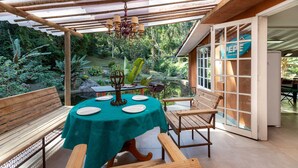 An outdoor patio with a wooden table and benches, surrounded by lush greenery and a view of a pond. - Boutique chalet amidst the Atlantic rainforest. (PETRÓPOLIS)