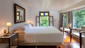 A bedroom with a bed, bedside tables, a mirror, a window with curtains, and a chair. - Boutique chalet amidst the Atlantic rainforest. (PETRÓPOLIS)