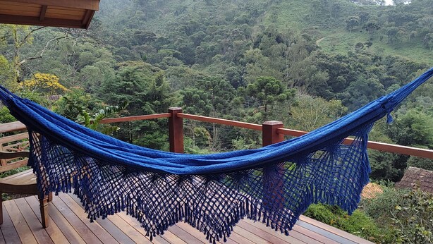 A hammock on a wooden deck with a view of a forested hillside. - Pousada Caminho do Escorrega (Itatiaia)