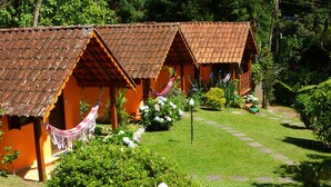 A row of rustic, terracotta-roofed cottages with hammocks and lush gardens. - Pousada Caminho do Escorrega (Itatiaia)