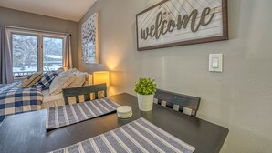 Ein Hotelzimmer mit einem Bett, einem Esstisch mit Platzsets, einer Topfpflanze und einem Schild mit der Aufschrift 'welcome' an der Wand.