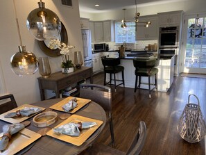 A modern kitchen with white cabinets, stainless steel appliances, and a dining area with a round table set for four. - Remodeled Colonial Retreat Close to  Shops and Dining (Wichita)