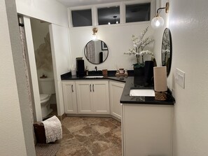 A bathroom with a white vanity, black countertop, and a mirror. There is a towel rack, a sink, and a toilet visible. - Remodeled Colonial Retreat Close to  Shops and Dining (Wichita)