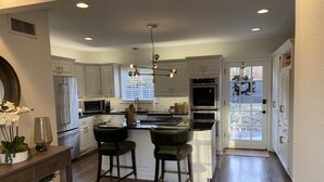 A modern kitchen with white cabinets, stainless steel appliances, and a central island with bar stools. - Remodeled Colonial Retreat Close to  Shops and Dining (Wichita)
