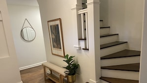 A staircase with wooden steps and white railings, a wooden bench, a potted plant, a framed picture, and a mirror on the wall. - Remodeled Colonial Retreat Close to  Shops and Dining (Wichita)