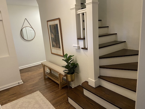 A staircase with wooden steps and white railings, a wooden bench, a potted plant, a framed picture, and a mirror on the wall. - Remodeled Colonial Retreat Close to Shops and Dining (Wichita)