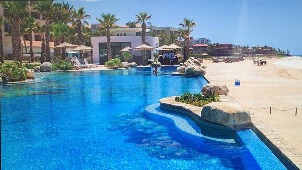Zwembad van een resort met uitzicht op het strand, met palmbomen en een heldere lucht.