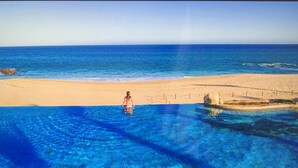 Een zwembad met helderblauw water, een zandstrand en iemand die in het water staat.