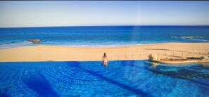 A pool with clear blue water, a sandy beach, and a person standing in the water. - Two Bedroom Spacious Ocean Front in Cabo (San José del Cabo)
