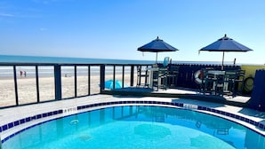 A swimming pool with a view of the beach, a deck area with outdoor seating, and a lifeguard stand. - Symphony Beach Club (Ormond Beach)