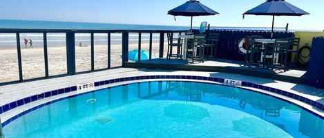 A swimming pool with a view of the beach, a deck area with outdoor seating, and a lifeguard stand.