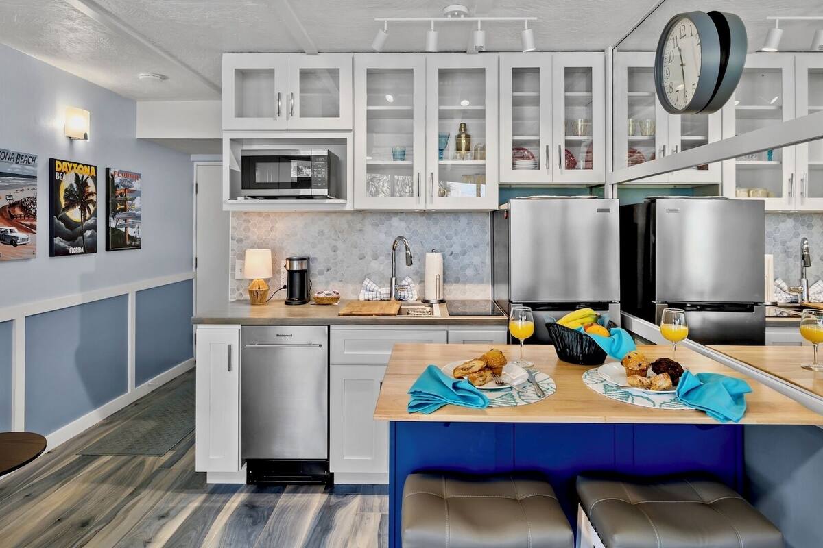A modern kitchen with white cabinets, a microwave, a coffee maker, and a dining area with a bench and table set for breakfast.