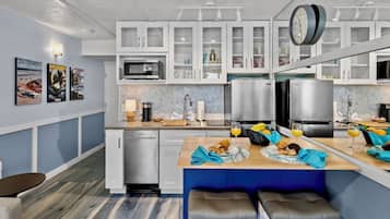 A modern kitchen with white cabinets, a microwave, a coffee maker, and a dining area with a bench and table set for breakfast.
