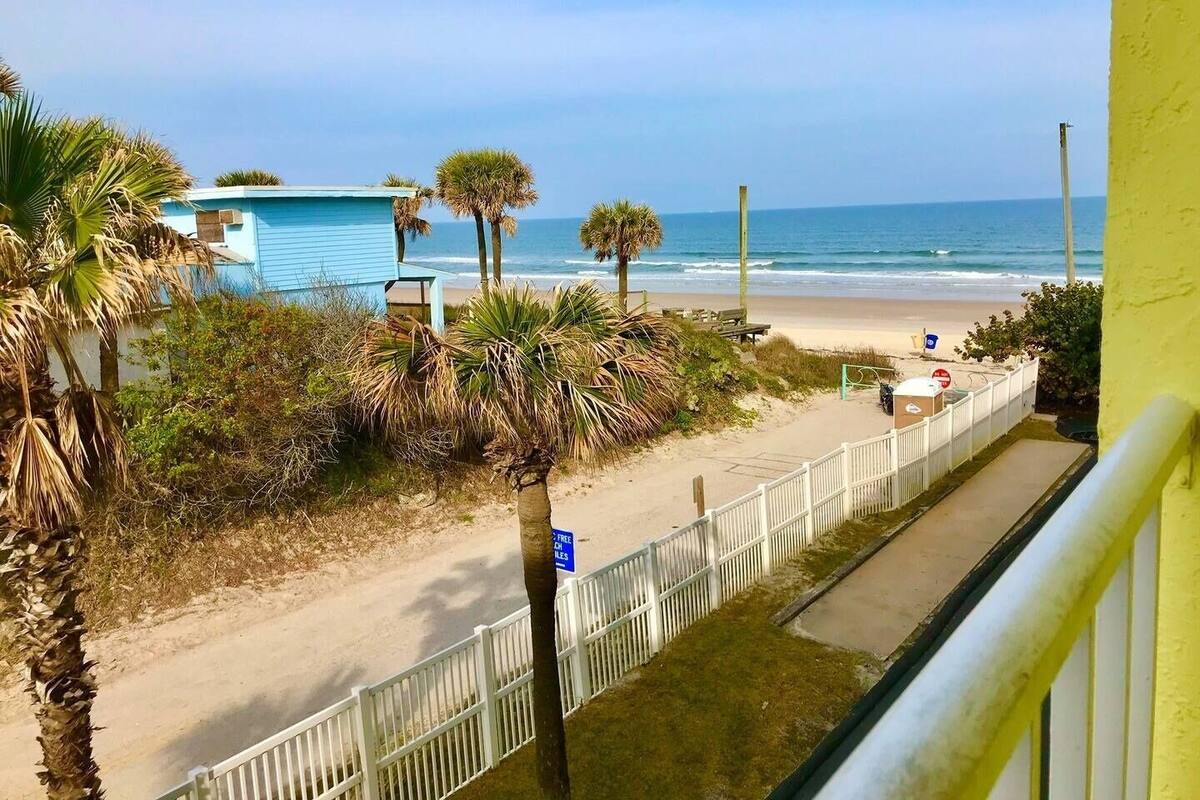 A beach view with a white fence, palm trees, and a blue building.