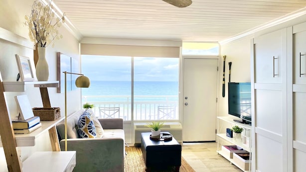 A modern living room with a view of the ocean, a ceiling fan, and a large window. - Symphony Beach Club (Ormond Beach)