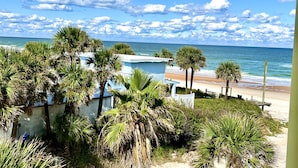 A beach view with palm trees, a white building, and the ocean. - Symphony Beach Club (Ormond Beach)