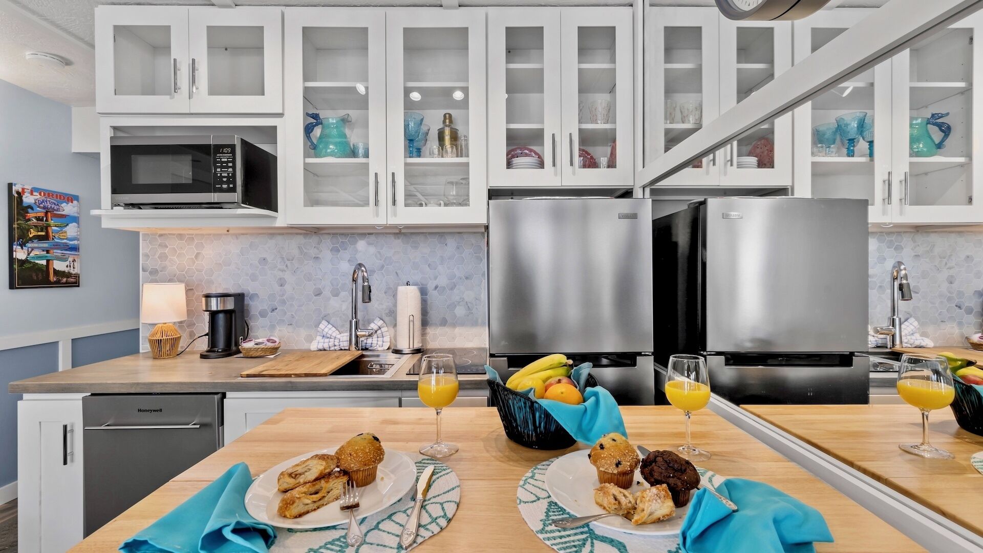 Una cocina moderna con gabinetes blancos, electrodomésticos de acero inoxidable y una zona de desayuno con muffins y jugo de naranja.
