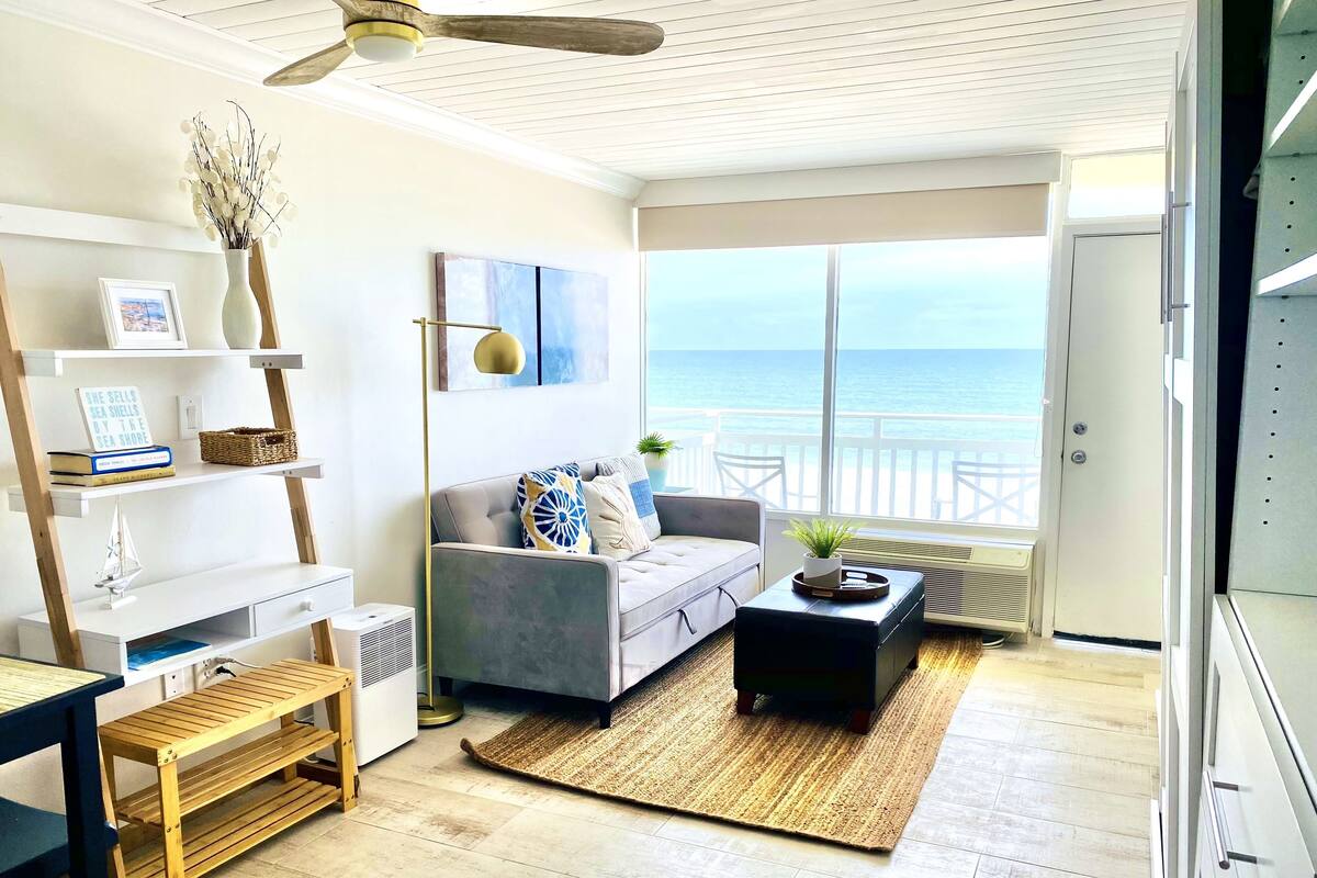 A modern living room with a view of the sea, a ceiling fan, and a large window.