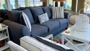 A modern living room with a grey sofa, a white armchair, and a glass coffee table. There are two lamps on the table and a white lantern on the floor. - Symphony Beach Club (Ormond Beach)