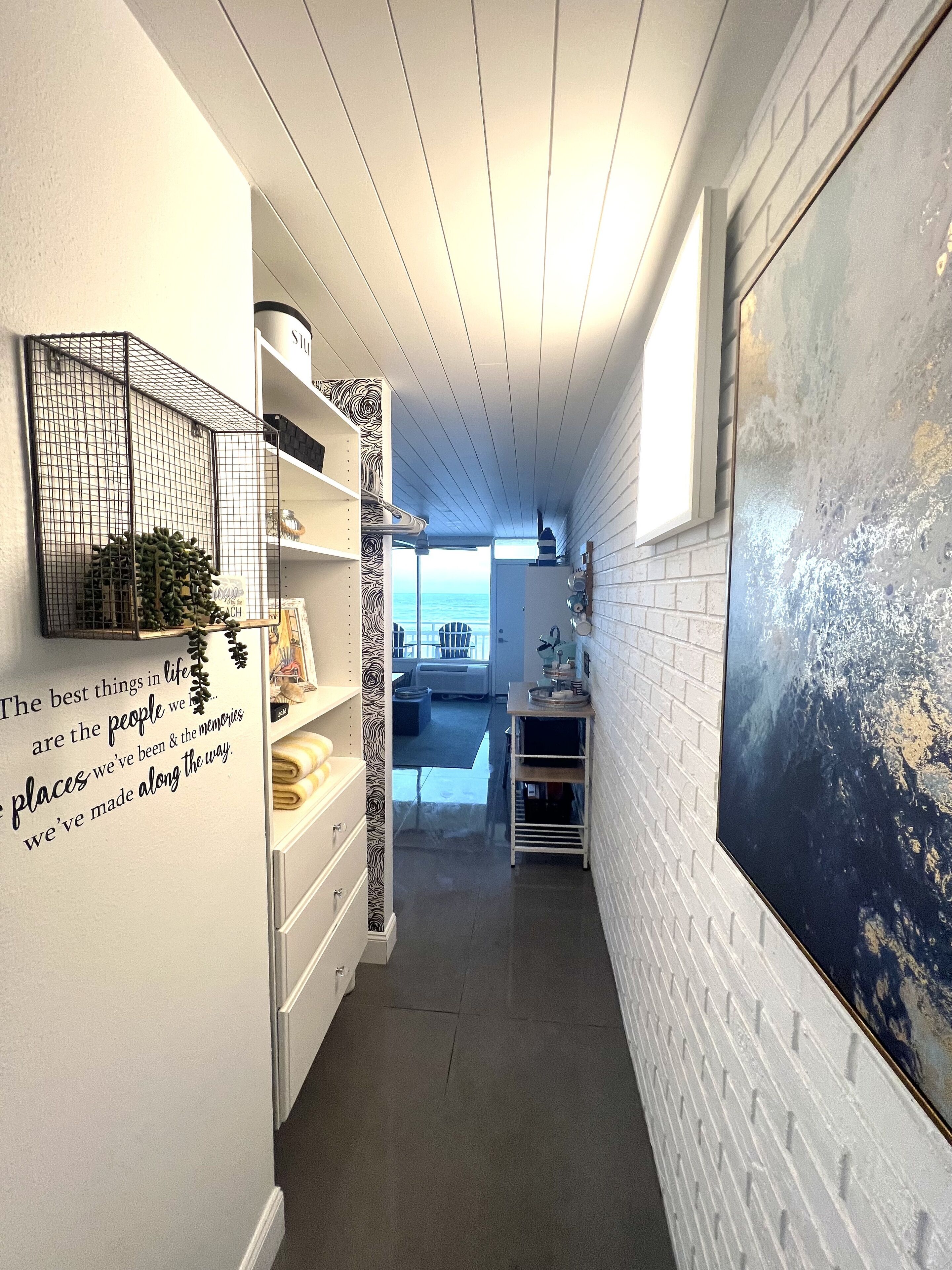 A narrow hallway with white brick walls, a large abstract painting, and a metal cage with plants.