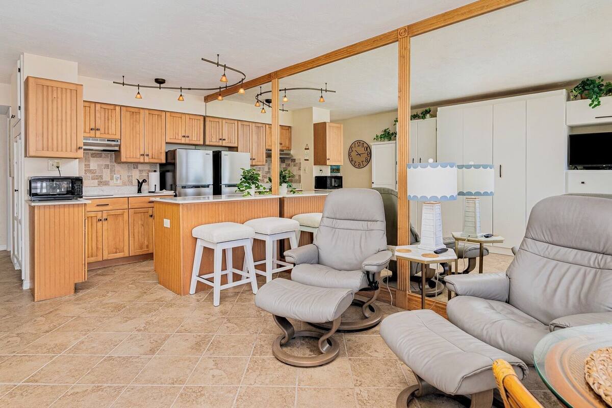 A modern kitchen with wooden cabinets, a central island, and a dining area with two bar stools.
