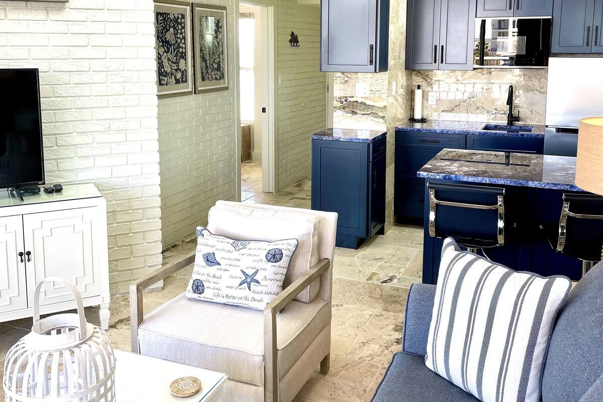 A compact living space with a kitchenette, a white brick wall, a flat-screen TV, and a cozy seating area with a patterned rug.