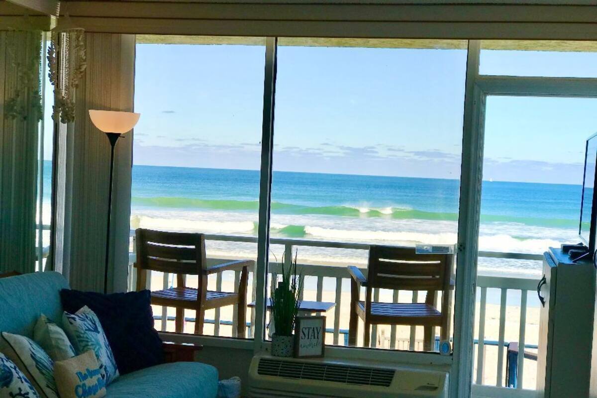 A room with a view of the beach, a sofa, a table, and two chairs.
